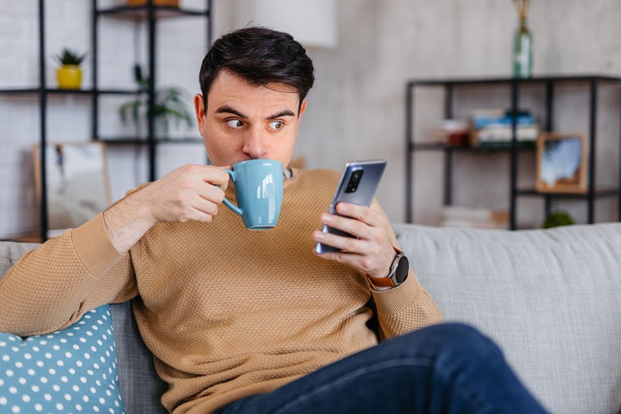 Man Skeptically Looks at His Phone While Drinking From a Mug