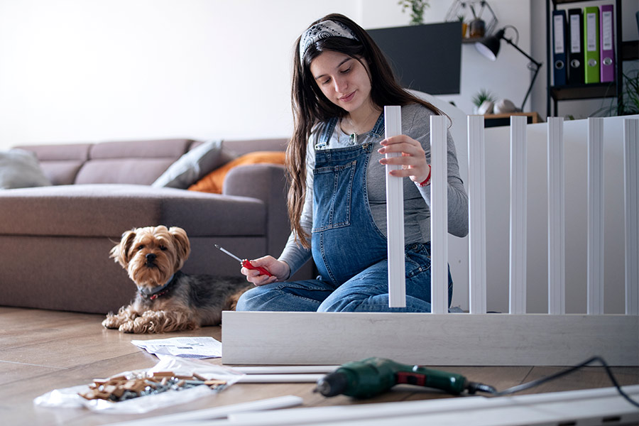 Pregnant Woman Kneeling on the Floor Building Baby Crib with a Yorkie Terrier Nearby