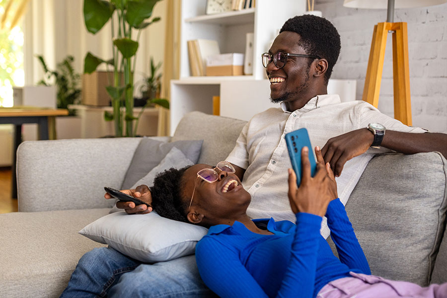 Young Man and Woman Laughing While Watching TV on the Couch